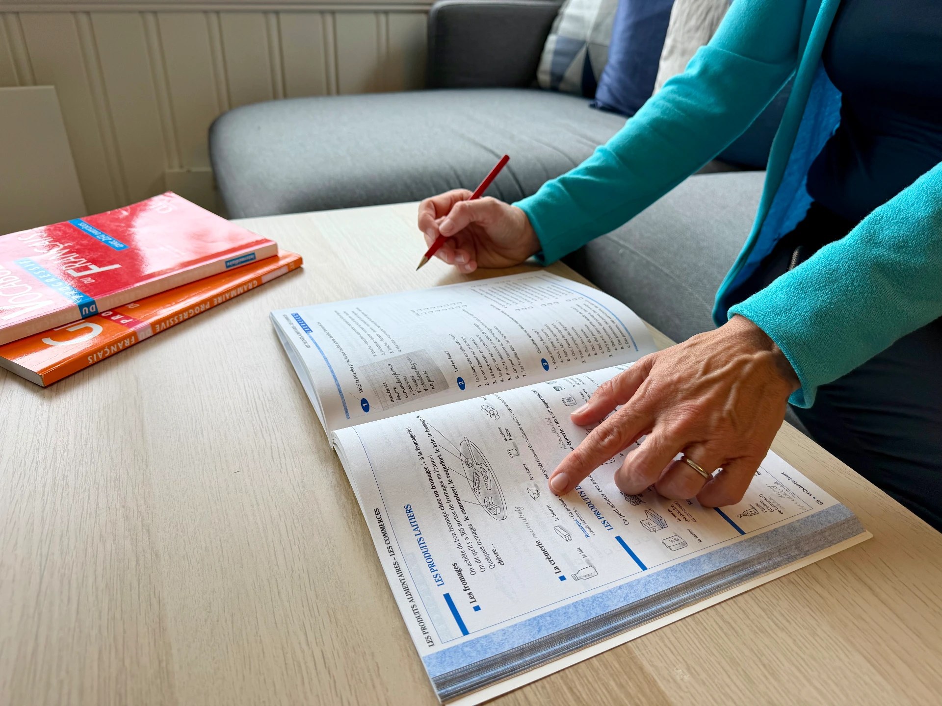 Åpen fransk arbeidsbok på et bord, med hånd som peker og blyant